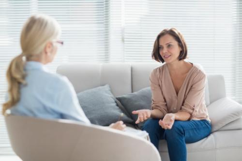 a woman sits on a couch talking to her therapist about addiction therapy programs who is sitting in a chair across from the patient