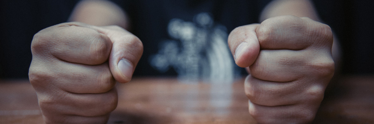 Two clenched fists rest on a wooden surface, side by side, embodying the tension often released at a mental health retreat in Boston. The dark, blurred background focuses attention on the hands, symbolizing the journey towards serenity.
