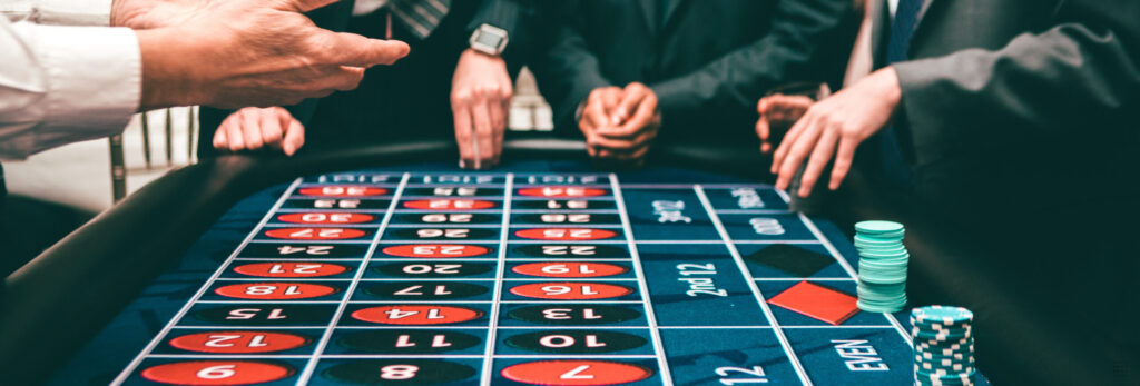 People in suits gather around a casino roulette table, placing bets with stacks of chips. A dealer’s hands gesture over the table, heightening anticipation and excitement—far from the calm one might find at a Mental Health Retreat in Boston.