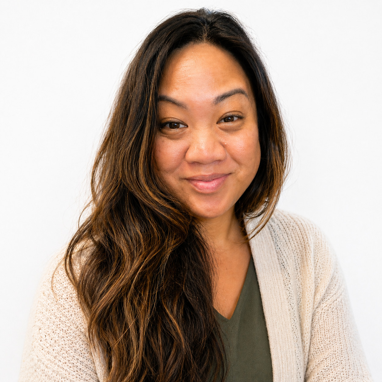 Meet The Staff: A woman with long, wavy brown hair and a light beige sweater smiles gently at the camera against a plain white background.